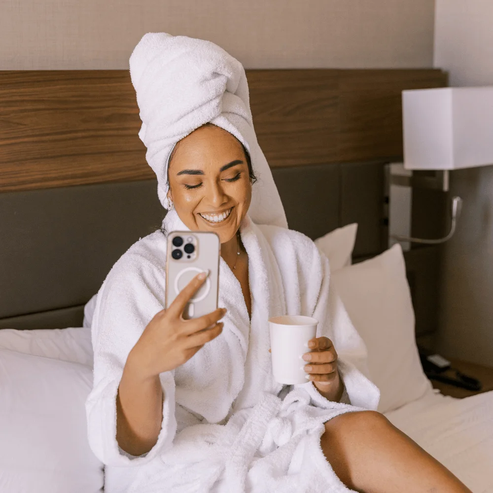 Woman in a white robe looking at her phone. Saturday self care ideas