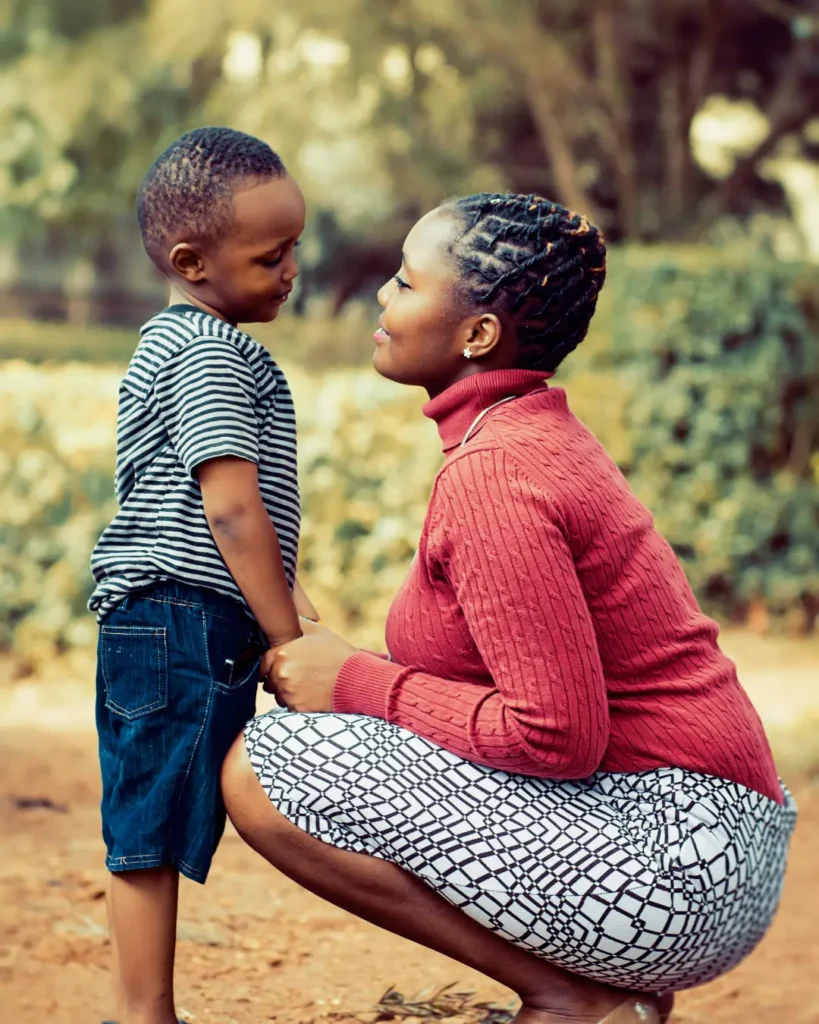 Tilt Shift Lens Photography of Woman Wearing Red Sweater and White Skirt While Holding a Boy Wearing White and Black Crew-neck Shirt and Blue Denim Short.1