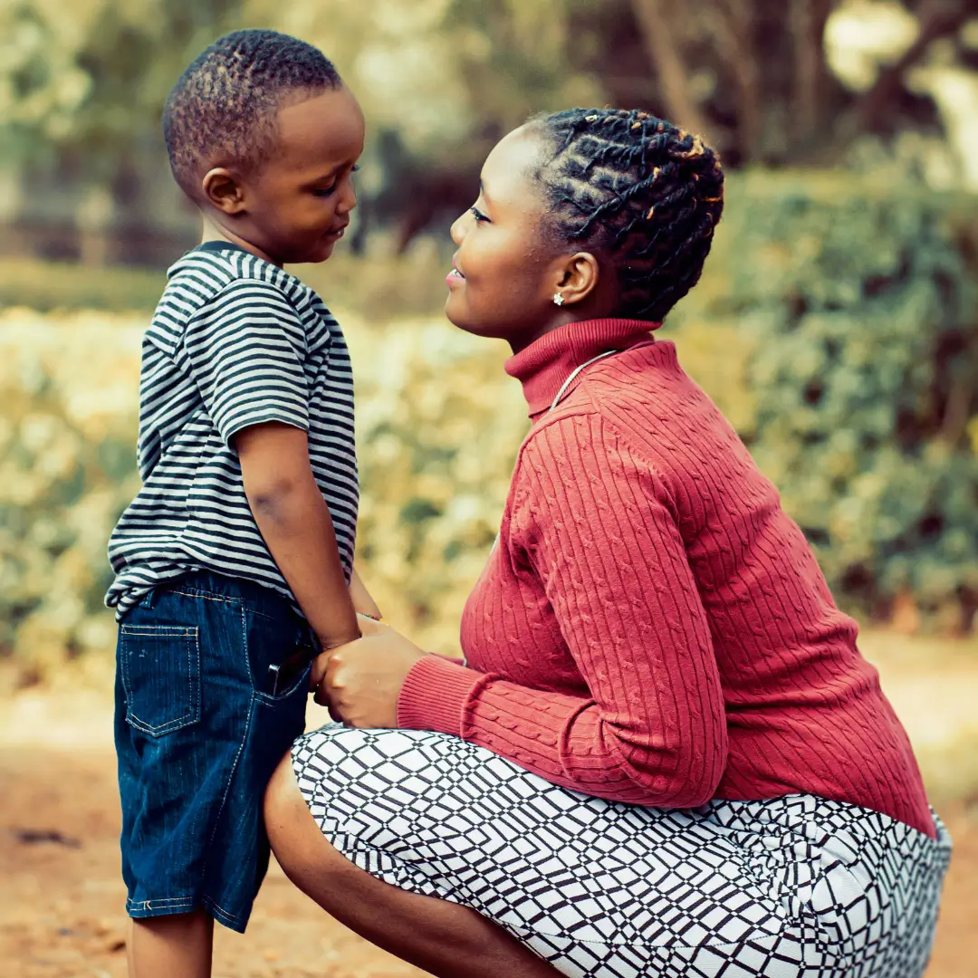 Tilt Shift Lens Photography of Woman Wearing Red Sweater and White Skirt While Holding a Boy Wearing White and Black Crew-neck Shirt and Blue Denim Short