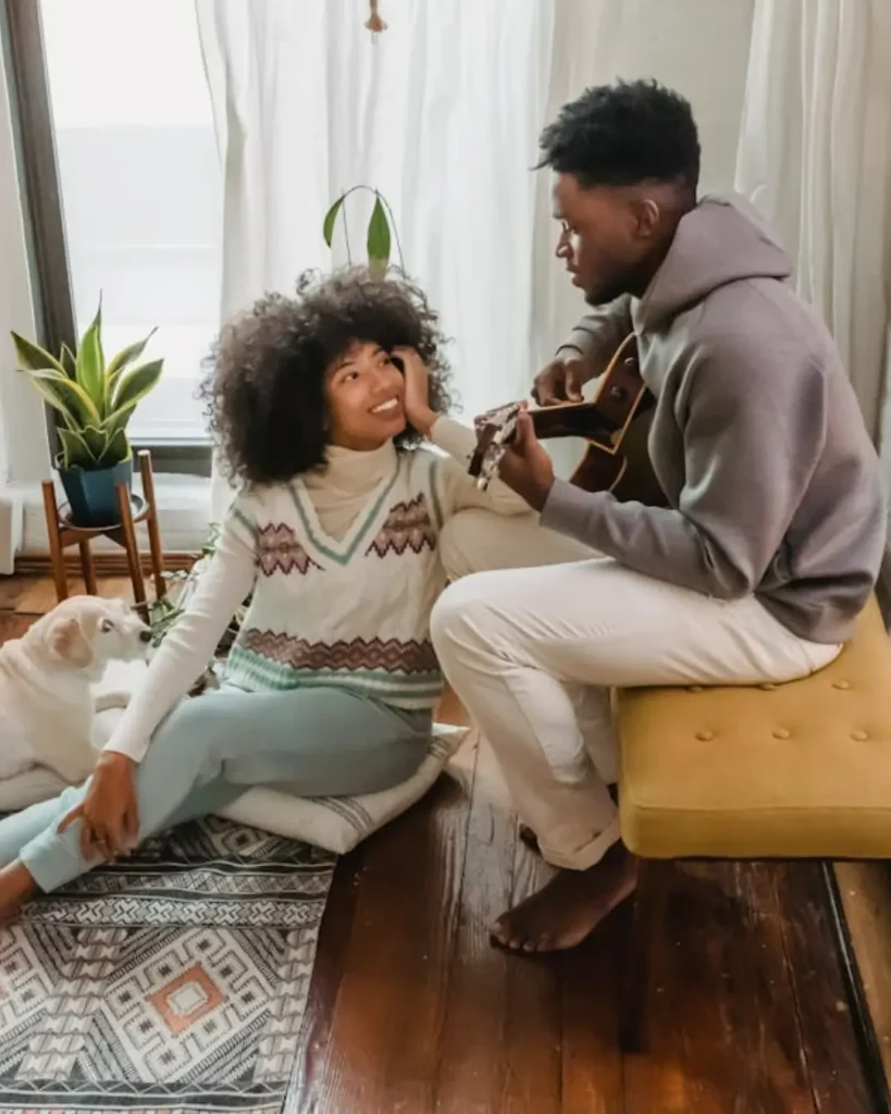 Black man playing guitar for girlfriend in room with dog