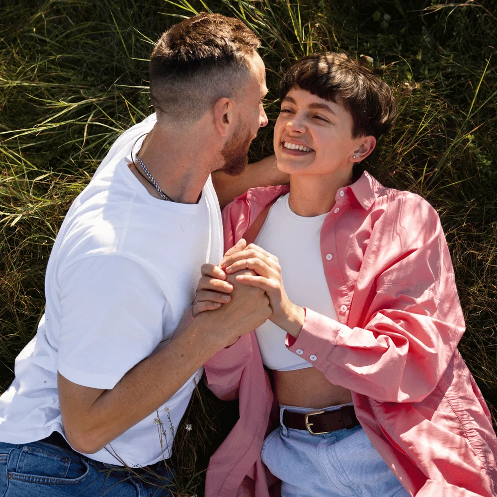 Couple smiling as they lay in grass. Journal Prompts For Couples