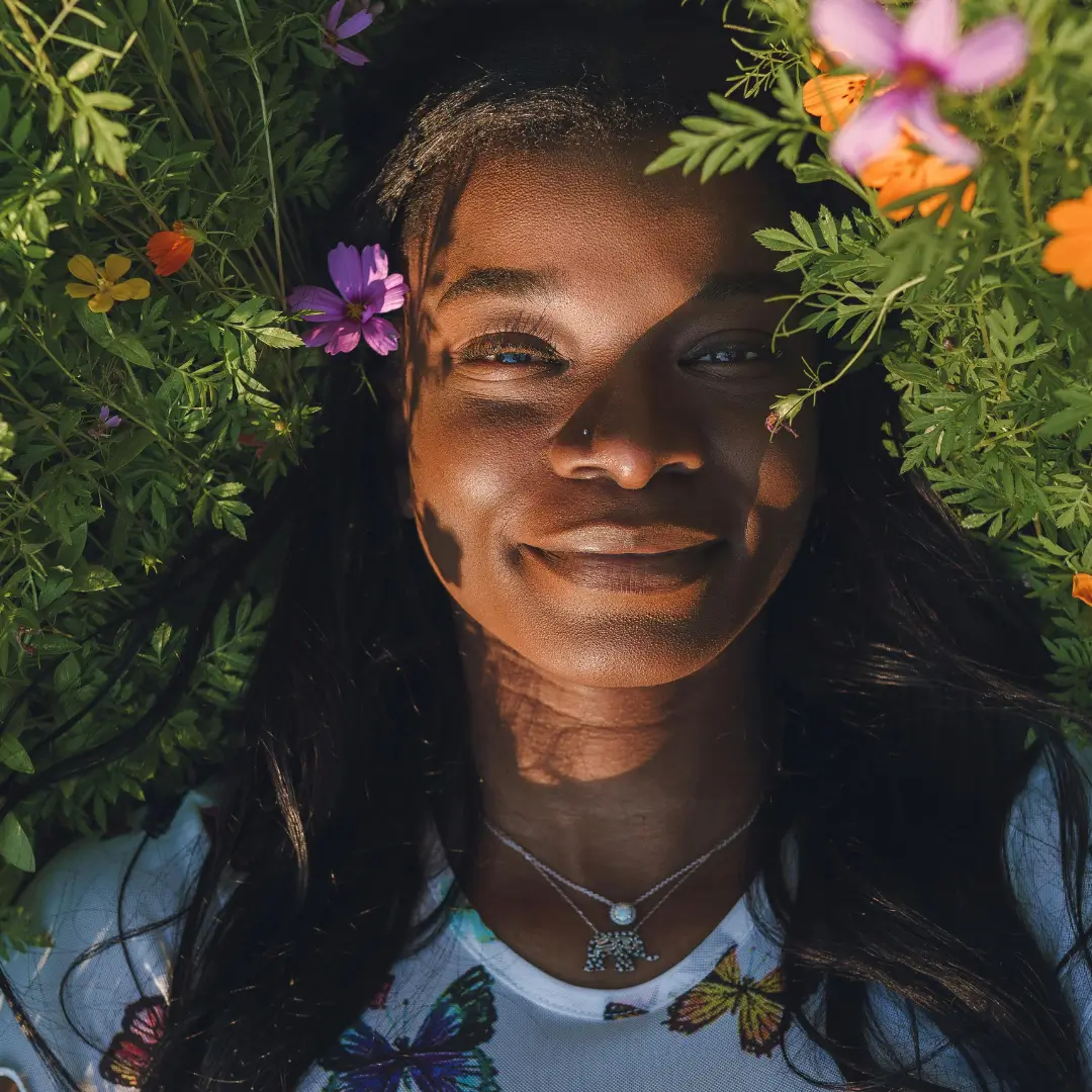 Happy black woman lying on grass with flowers