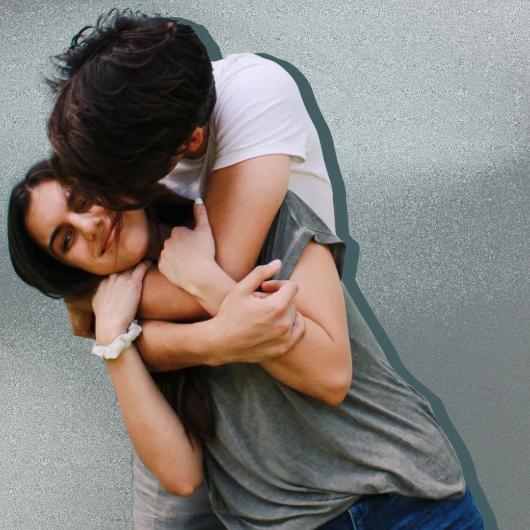 Man hugging a woman from behind and kissing her on her cheek. InordinateAffection