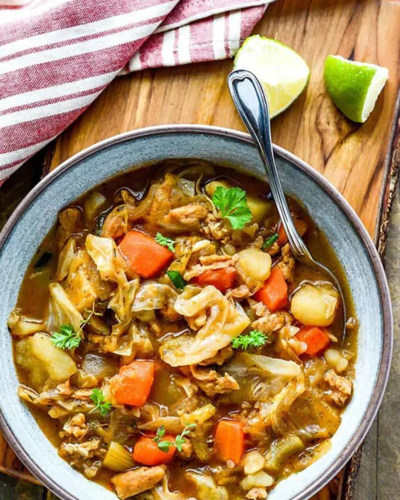 A grey bowl, with Ital stew and fresh vegetables.