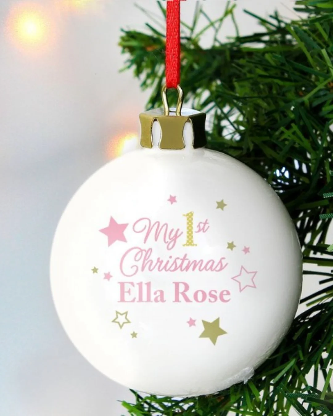 A white ceramic bauble with pink and gold stars, with the personalisation 'My 1st Christmas Ella Rose'