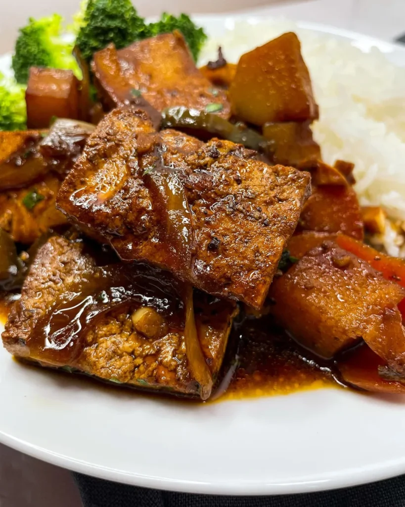 A plate, with Tofu brown stew chicken, white rice and broccoli.