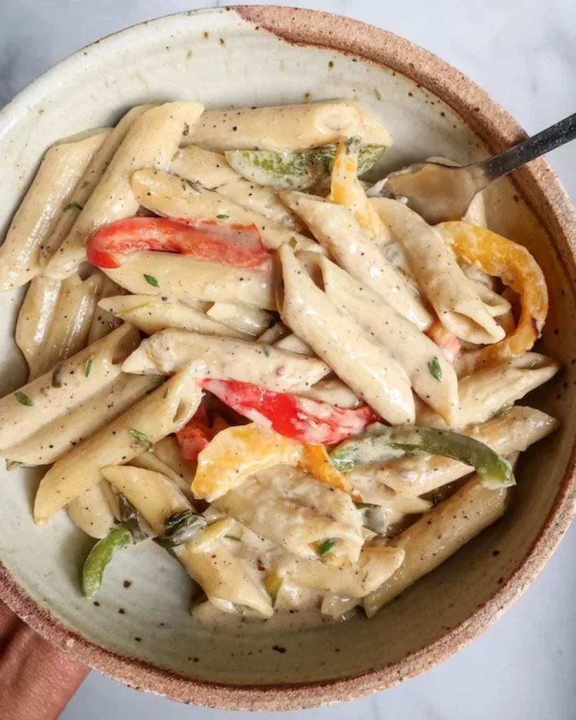 A bowl of pasta in a creamy sauce, with yellow, green and red bell peppers.
