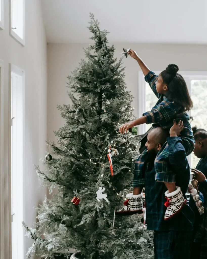 A Girl Putting A Christmas Star On A Christmas Tree