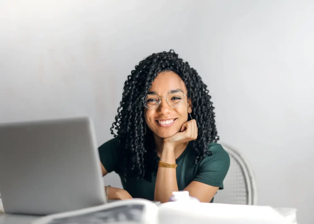 Happy ethnic woman sitting at table with laptop.