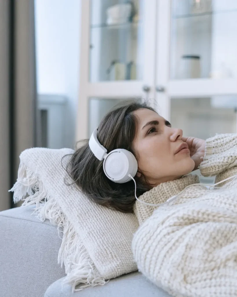 A Woman in a Knitted Sweater Listening to Music while Lying Down on a Couch