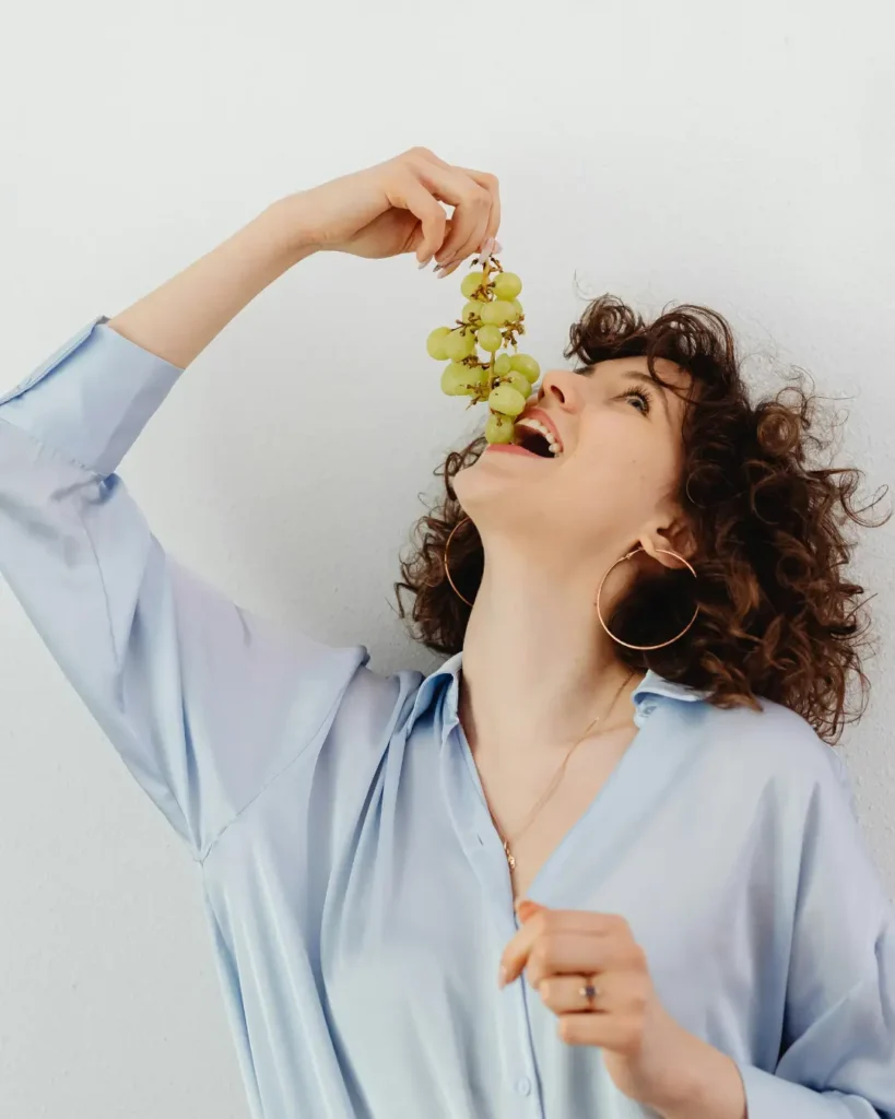 A Woman with Curly Hair Wearing Blue Long Sleeves while Eating Green Grapes