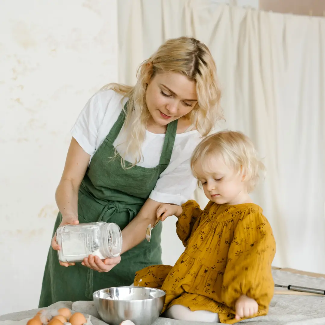 Woman cooking near little cute girl on table