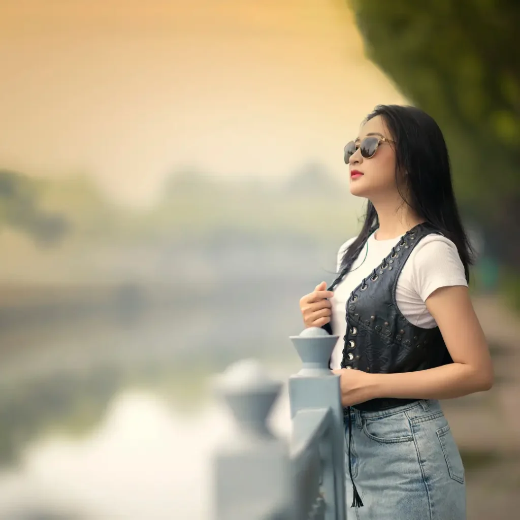 Self assured young ethnic lady standing near river under sundown sky