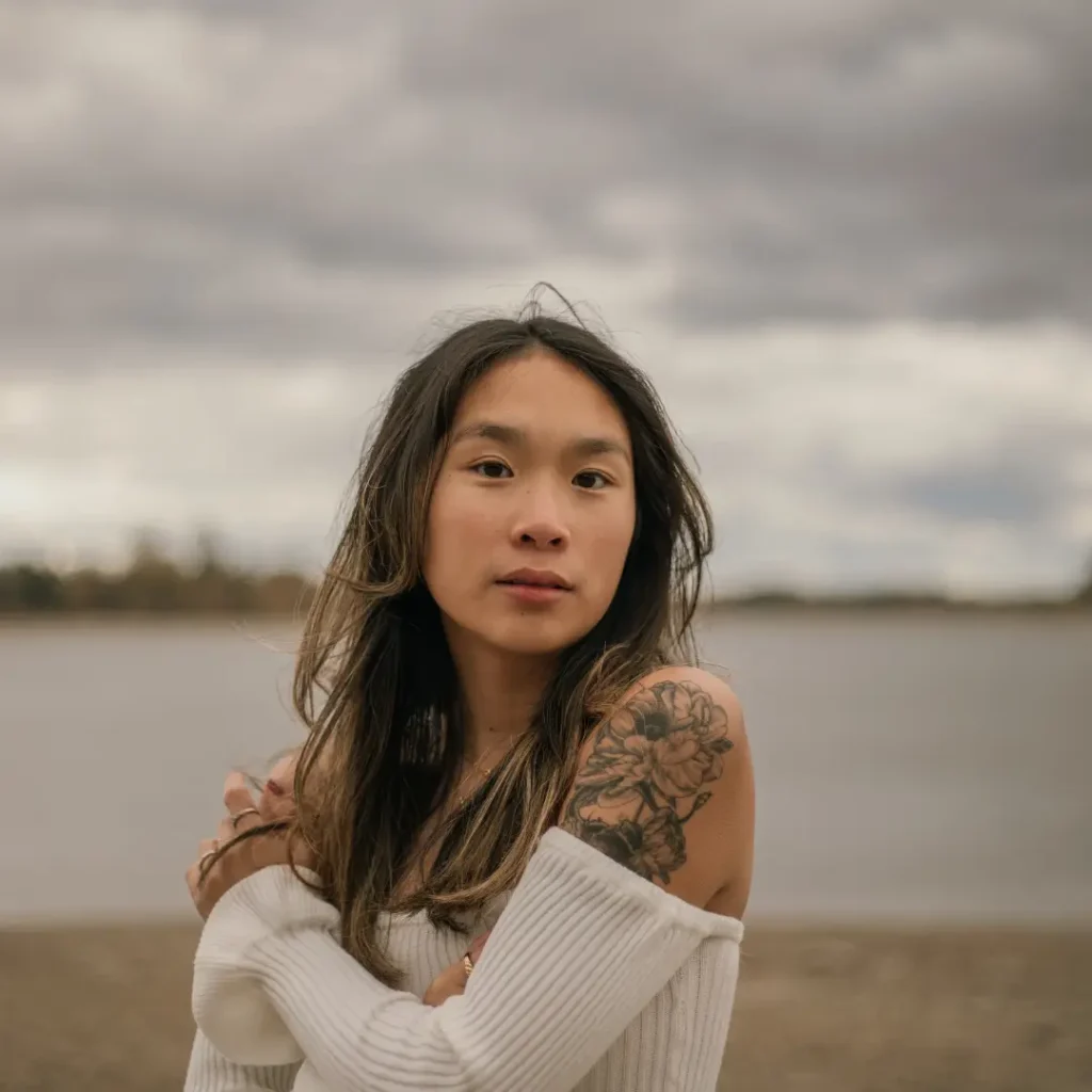 Woman in Sweater Standing on Shore Hugging Self