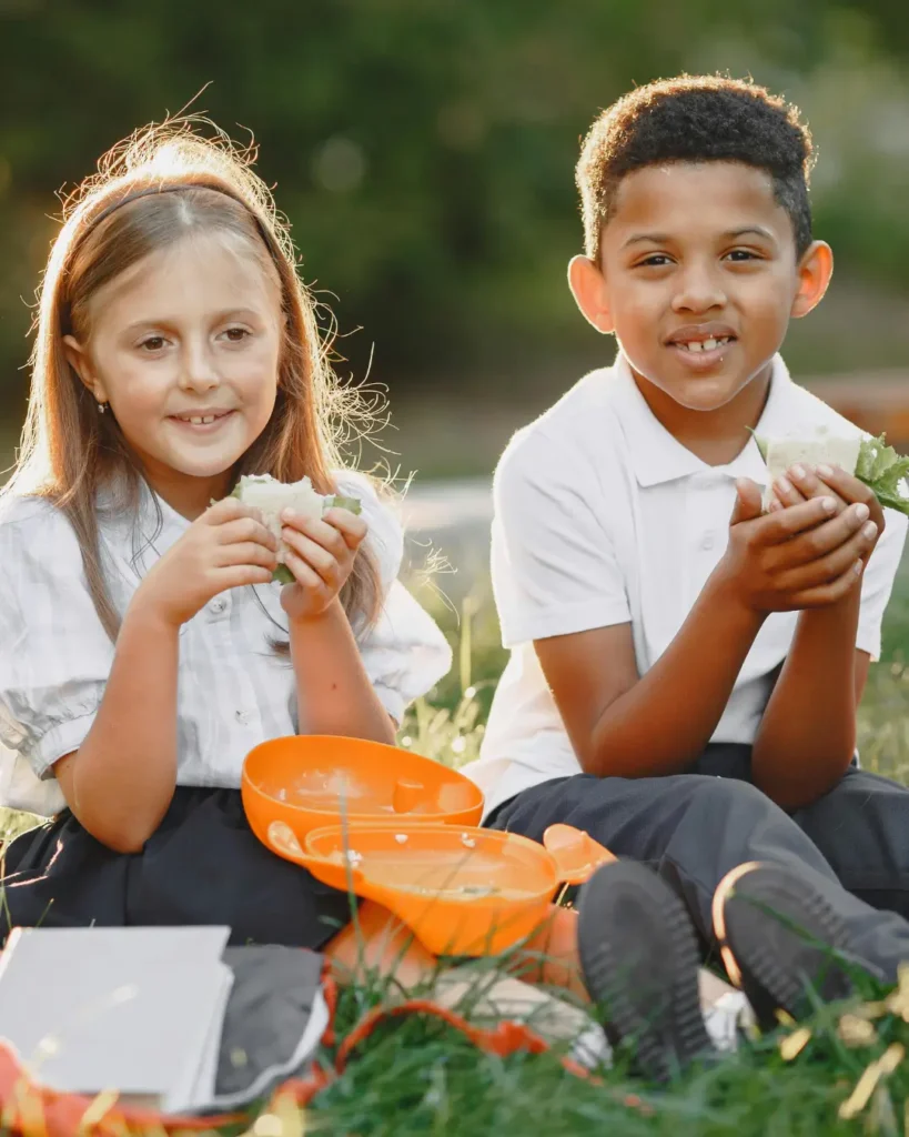 Happy Kids Sitting on Grass Eating Lunch
