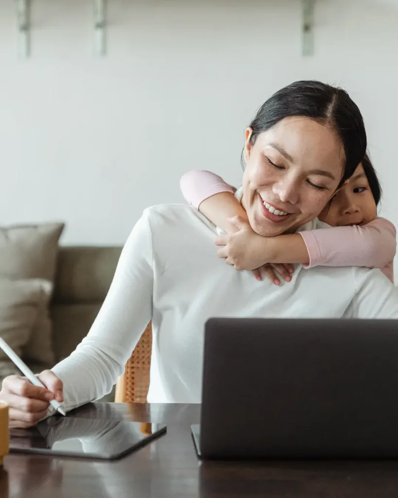 Happy mother working from home and little daughter hugging mom