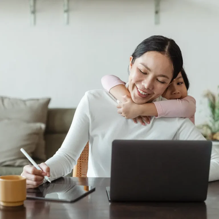 Happy mother working from home and little daughter hugging mom