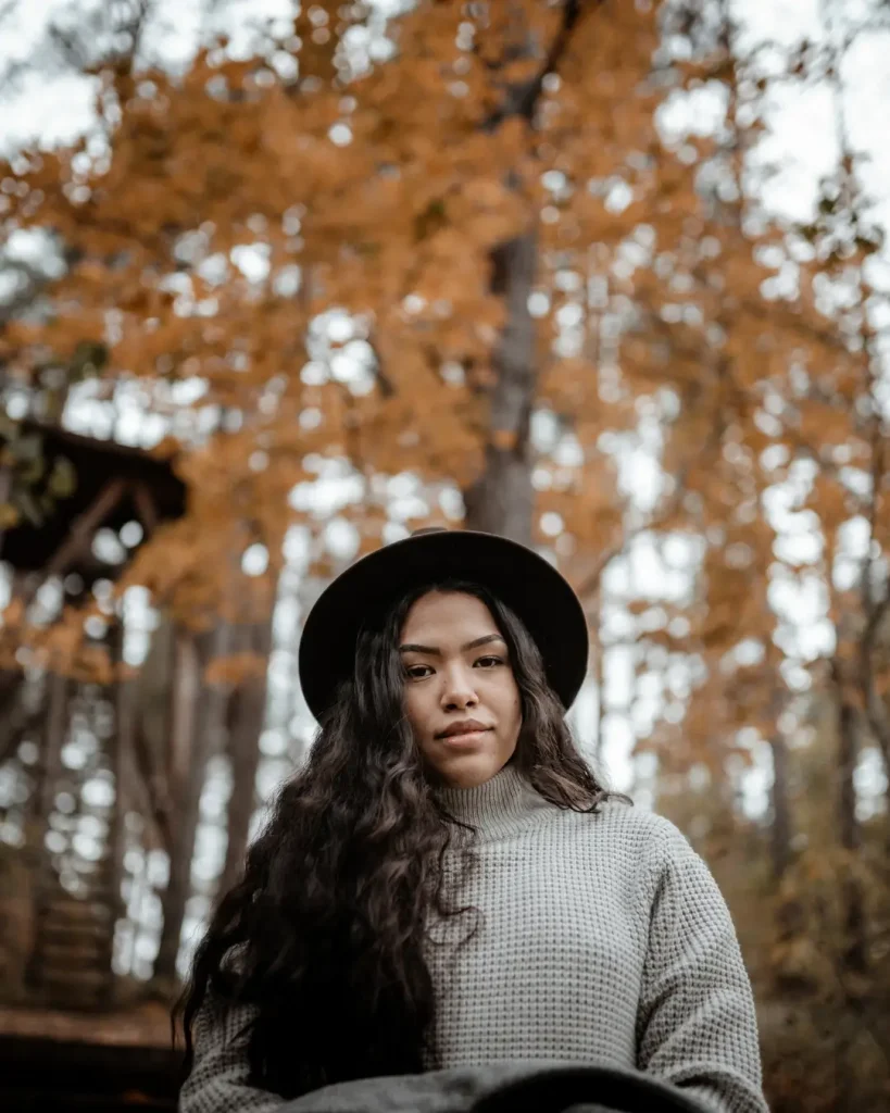 Positive ethnic woman resting on bench in autumn park